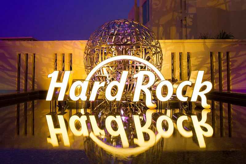 A glowing Hard Rock sign is displayed in front of a reflective water surface at night.